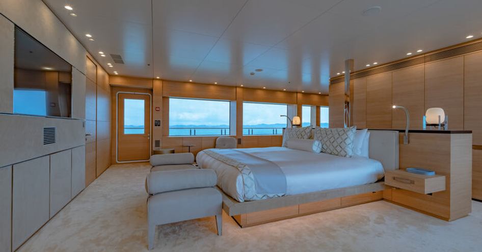 Overview of full-beam master cabin onboard superyacht WANDERLUST. Central berth facing portside of image, with vast glazing in background. 