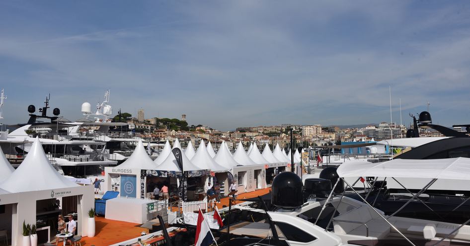 Exhibition tents lined up along dockside at Cannes Yachting Festival, yachts moored adjacent.