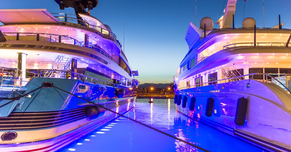 Aft view of a pair of moored superyachts at dusk, lit by neon blue lighting at Port of Antibes