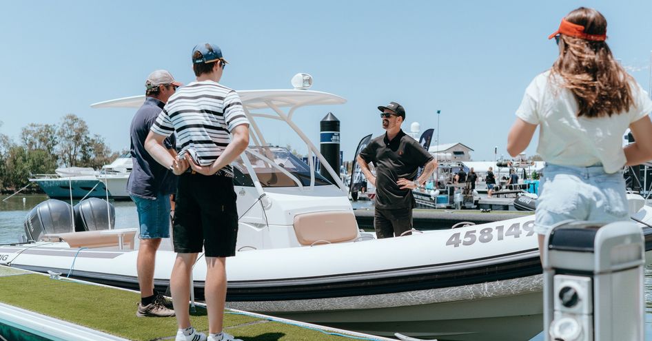 Representative in fishing boat talking to visitors on the dock at Sanctuary Cove Boat Show.