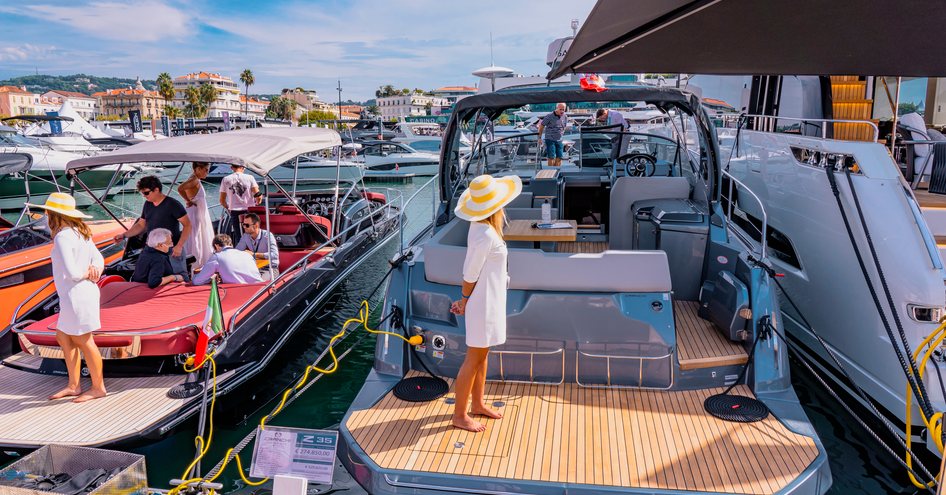 Lady in white dress and yellow sunhat standing on small yacht berthed at Cannes Yachting Festival. Bordered by other berthed yachts.