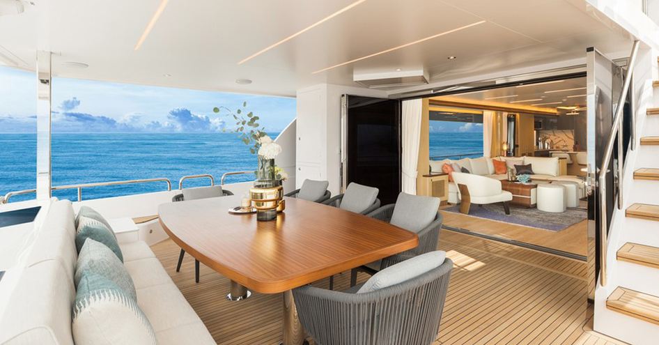 Aft deck onboard Horizon FD80. Seating around alfresco dining option, adjacent to door leading to interiors. Surrounded by sea.