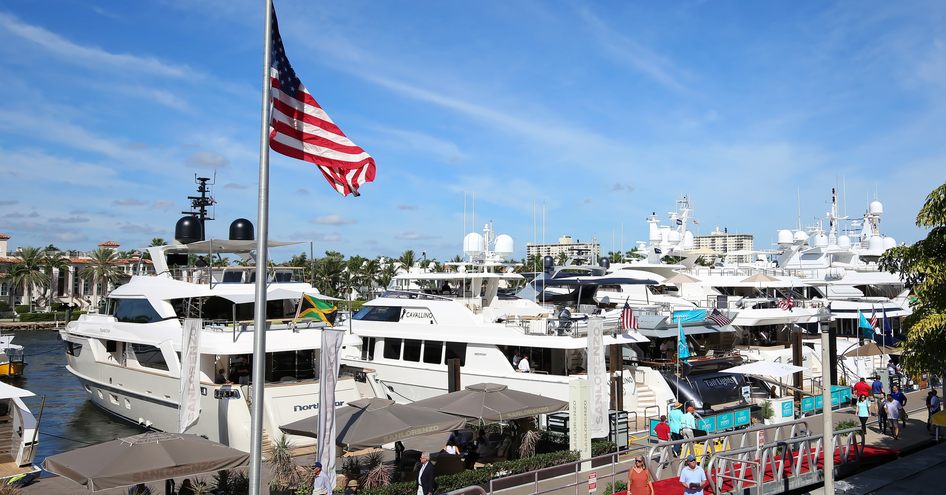 American flag flying at FLIBS next to marina and red carpet, motoryachts moored in background