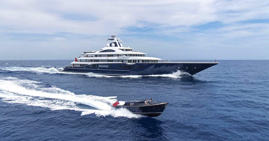 Small tender boat moving at speed on sea with large superyacht in background