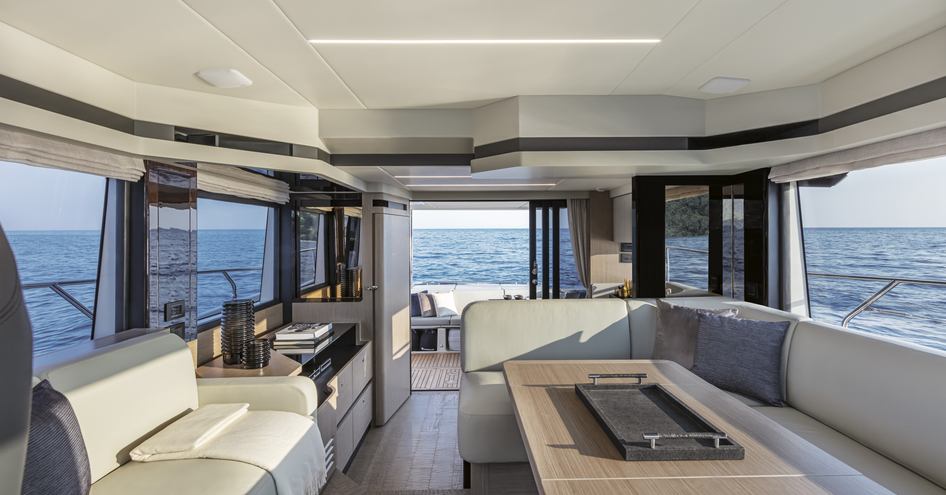 Main salon onboard Absolute 50Fly, sofas line either side with dining table to starboard side, surrounded by wide windows, overlooking aft deck