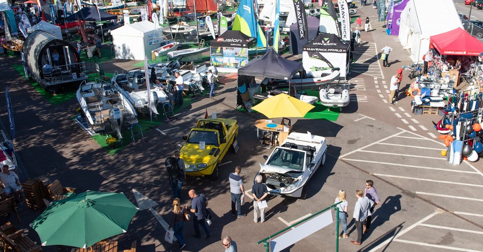 Mayflower Park at the Southampton Boat Show. Exhibitor stands and parasols throughout car park with visitors walking around.