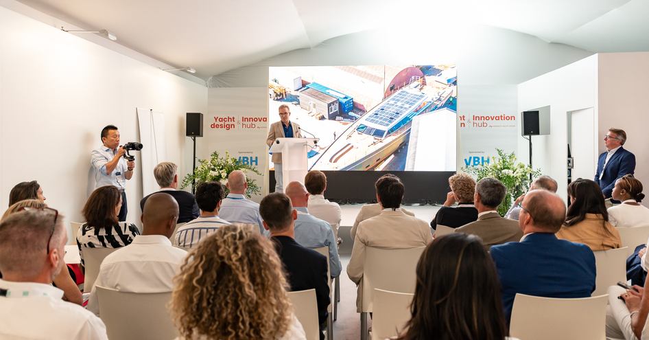 Overview a seminar taking place at the Yacht Design & Innovation Hub during the Monaco Yacht Show. Visitors seated watching a slideshow and speaker on the stage.