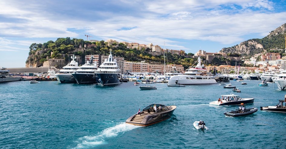 Tender cruising in to Port Hercule, Monaco. Multiple motor yachts moored around the marina with buildings visible in the background.