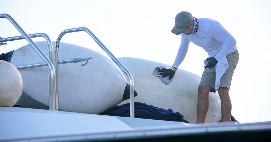 A man bent over cleaning a yacht with a cloth.