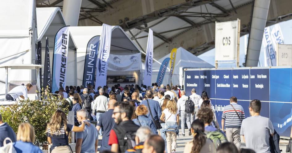 Visitors to the Genoa International Boat Show walking towards an entrance by exhibitor flags