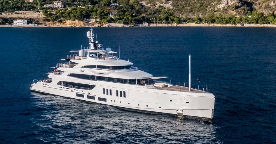 Elevated view of M/Y CALEX at sea, with high cliff tops in background.