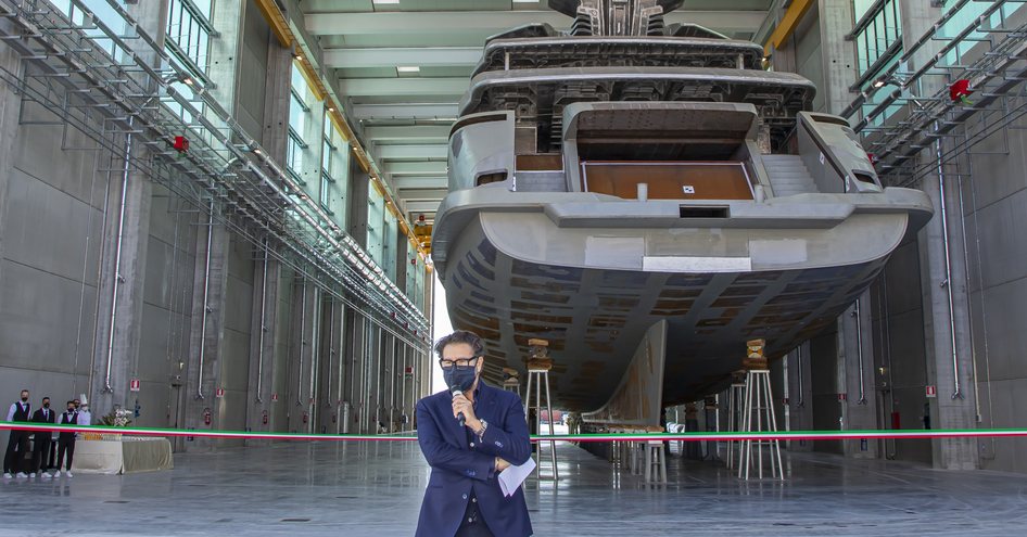 Man talking on microphone in front of ribbon and ship in background