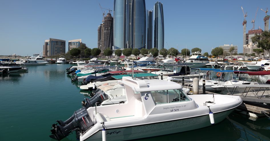 Overview of a marina in Abu Dhabi at water level, with boats berthed along pontoons and skyscrapers in the background