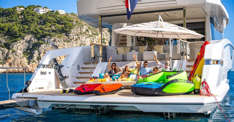 Family on beach club of Sunseeker 90 Ocean waving towards camera with toys in front