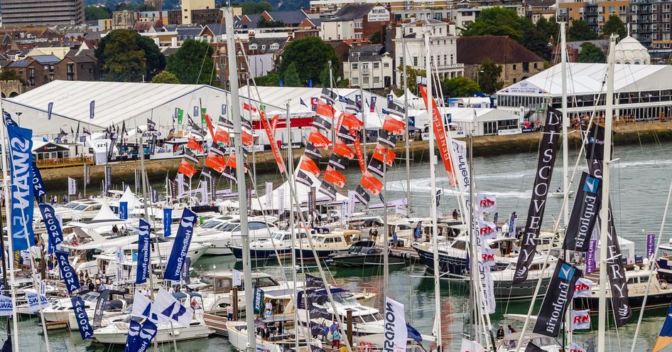 Overview of Mayflower Park marina at Southampton during boat show. Sailing boats and motor yachts berthed along docks with abundance of flags flying.