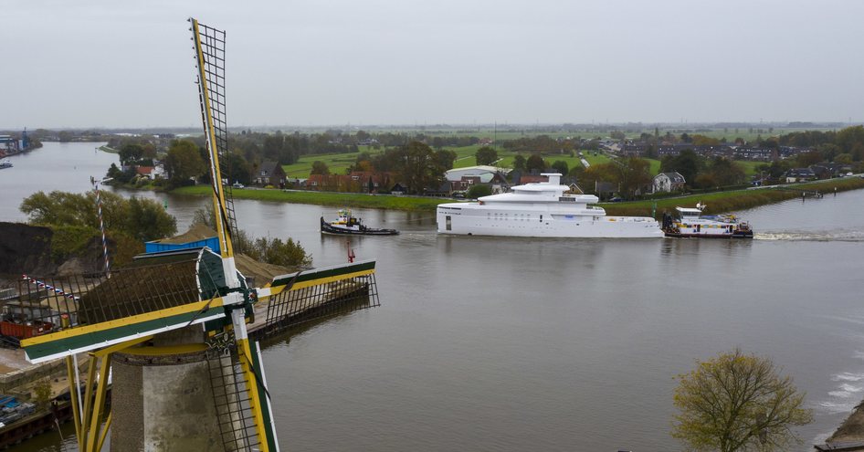 Feadship explorer yacht SHINKAI being towed up river by two tugboats, surrounded by windmill and green landscape