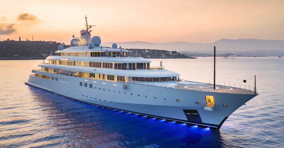 GOLDEN ODYSSEY by Lurssen shot at sunset with view over starboard bow and side profile whilst yacht on anchor in smooth sea, with land in background