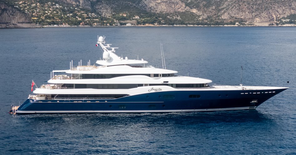 superyacht AMARYLLIS showing her blue hull and white superstructure in front of a mountainous backdrop