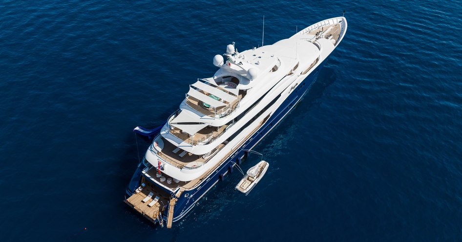 An aerial view of the stern/starboard-side of superyacht AMARYLLIS while at anchor in a dark blue sea