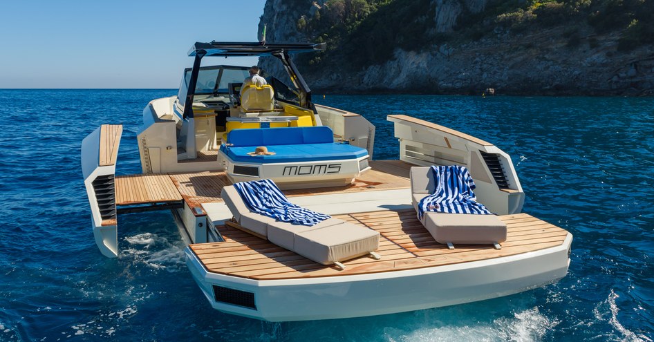 Aft view of Evo R4 XT anchored in a bay, with waterside terrace folded down and sun loungers on swim platform.